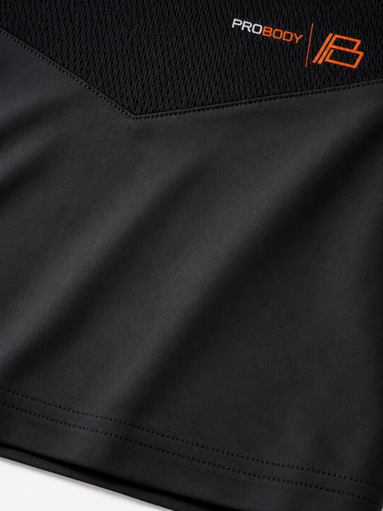 Close-up of the black ProBody performance tee shoulder showing the perforated mesh panel and the orange PROBODY B-mark